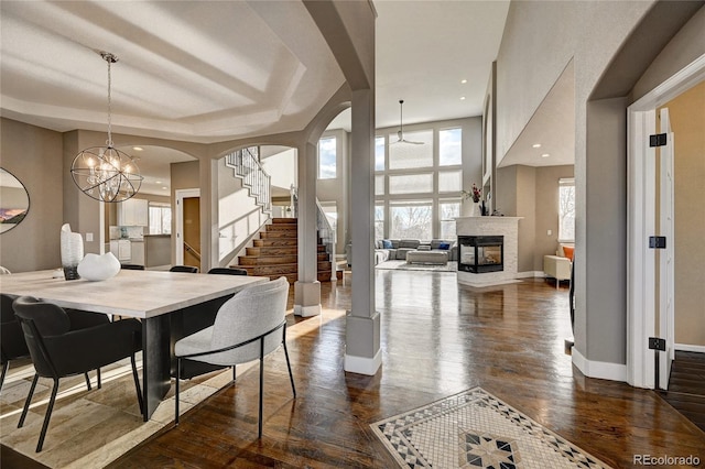 dining room featuring a multi sided fireplace, a raised ceiling, dark hardwood / wood-style floors, and a notable chandelier