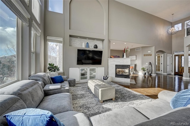 living room with a high ceiling, wood-type flooring, a notable chandelier, and a multi sided fireplace