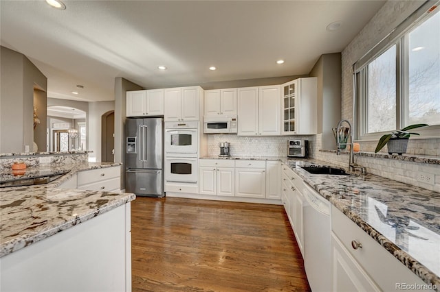 kitchen with white cabinetry, white appliances, dark wood-type flooring, light stone counters, and sink