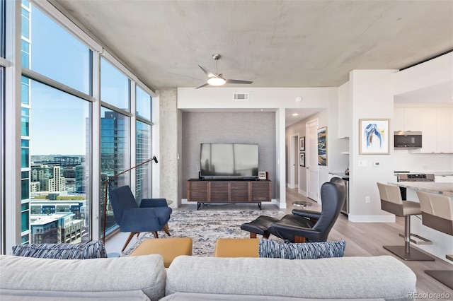 living room featuring light wood-style flooring, visible vents, baseboards, a ceiling fan, and a wall of windows