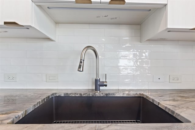 kitchen with wall chimney range hood, light stone counters, decorative backsplash, and a sink