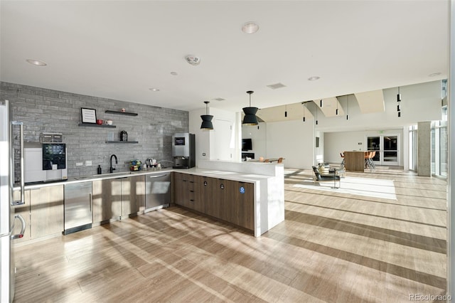 kitchen featuring open floor plan, a peninsula, light countertops, open shelves, and a sink