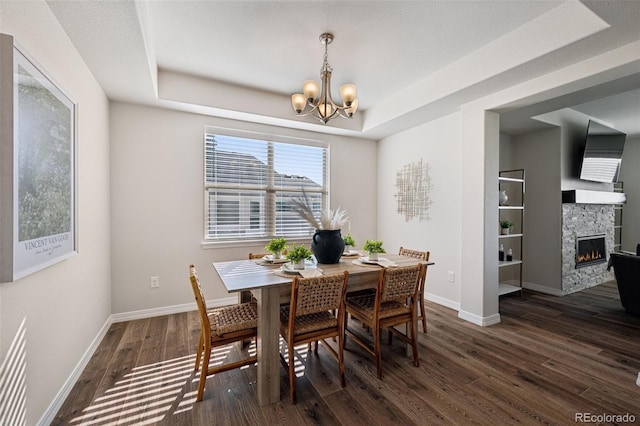 1871 Walnut Creek Ct, Colorado Springs, CO 80921 - dining space featuring dark wood-style flooring, a chandelier, a stone fireplace, and a raised ceiling