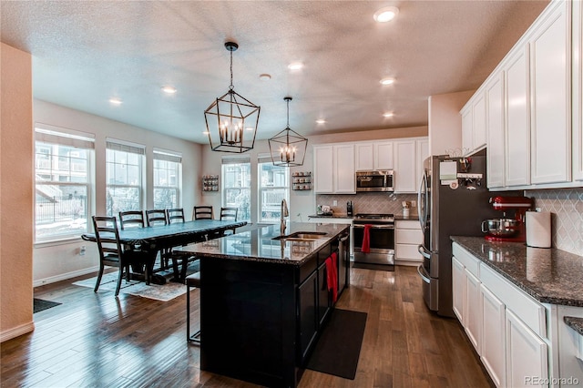 kitchen featuring pendant lighting, appliances with stainless steel finishes, white cabinets, a sink, and an island with sink