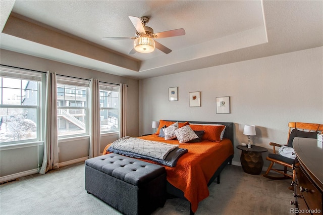 bedroom with a tray ceiling, light colored carpet, visible vents, and baseboards