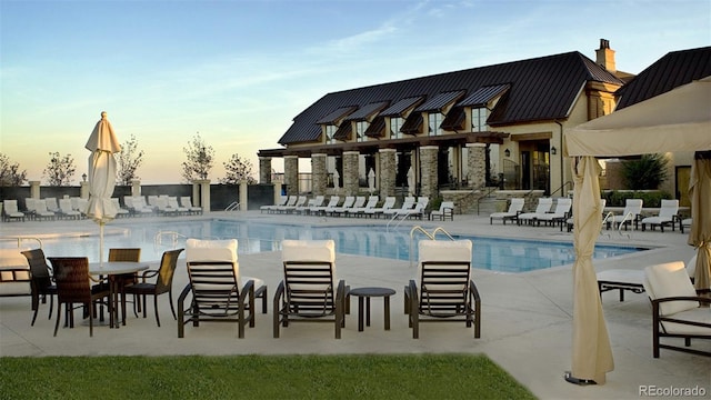 pool at dusk with a community pool and a patio