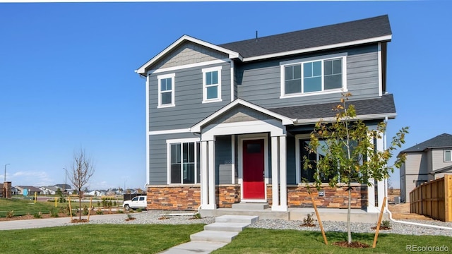 view of front of house with stone siding, a front yard, and a shingled roof