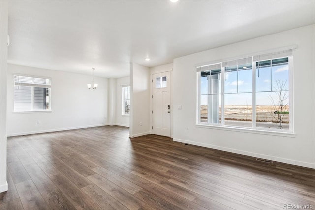 unfurnished living room with dark wood-style flooring, a chandelier, baseboards, and recessed lighting