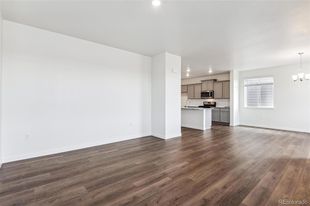 unfurnished living room featuring a chandelier, dark wood finished floors, baseboards, recessed lighting, and a sink