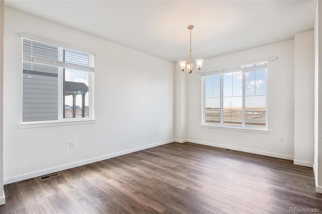 spare room with a chandelier, dark wood finished floors, and baseboards
