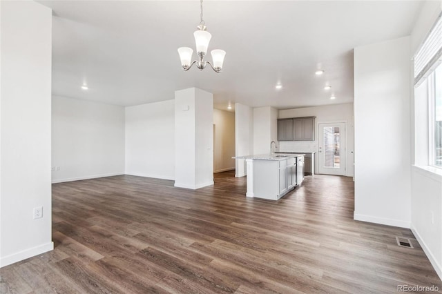unfurnished living room featuring a chandelier, healthy amount of natural light, dark wood-style flooring, recessed lighting, and baseboards