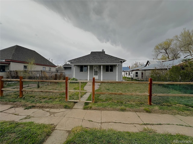 bungalow-style house with covered porch, a fenced front yard, a shingled roof, and a front lawn