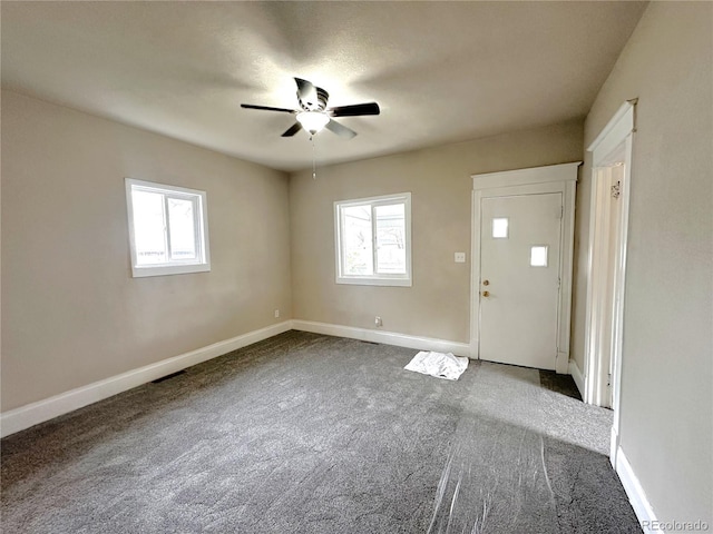 spare room featuring dark carpet, a ceiling fan, and a wealth of natural light