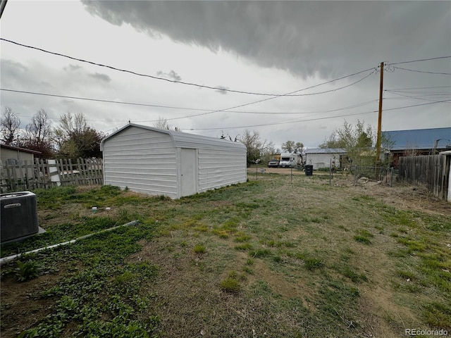 view of yard with central AC, an outbuilding, fence, and a storage shed