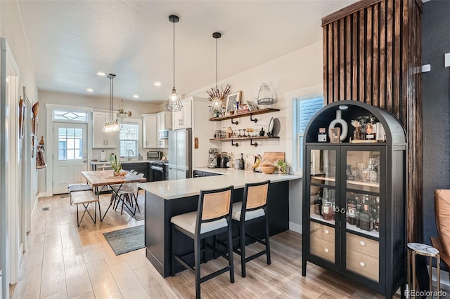 kitchen featuring pendant lighting, white cabinetry, fridge, a kitchen breakfast bar, and kitchen peninsula