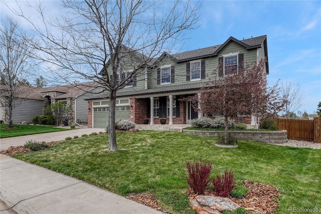 traditional-style house with a porch, driveway, a front yard, fence, and stone siding