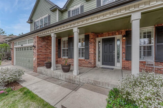 doorway to property with a porch, brick siding, driveway, and a garage