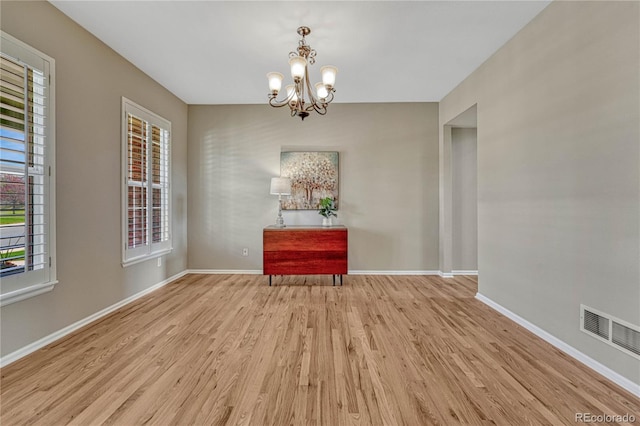 unfurnished dining area featuring baseboards, a chandelier, wood finished floors, and visible vents