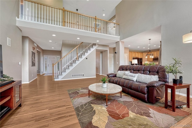 living area with a towering ceiling, visible vents, baseboards, light wood finished floors, and stairs