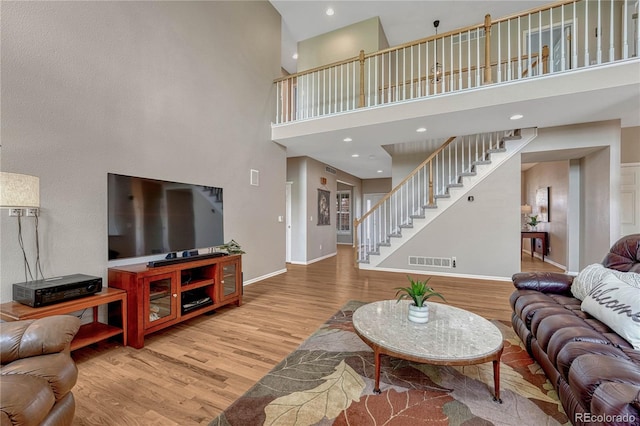 living room featuring a towering ceiling, visible vents, wood finished floors, stairway, and baseboards