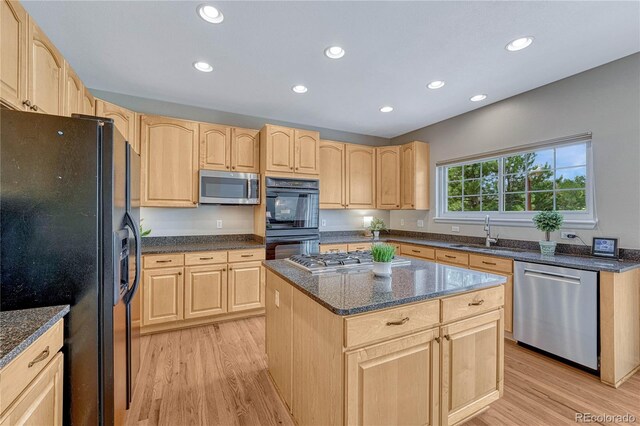 kitchen with a sink, light brown cabinetry, black appliances, and light wood finished floors