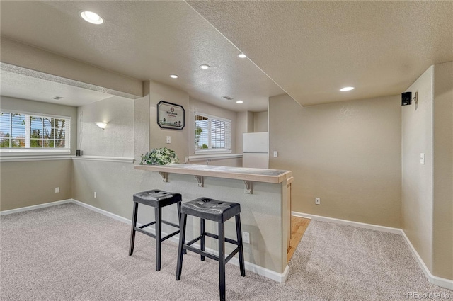 kitchen featuring freestanding refrigerator, a textured ceiling, and light carpet