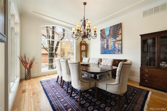 dining space featuring baseboards, light wood finished floors, visible vents, and crown molding