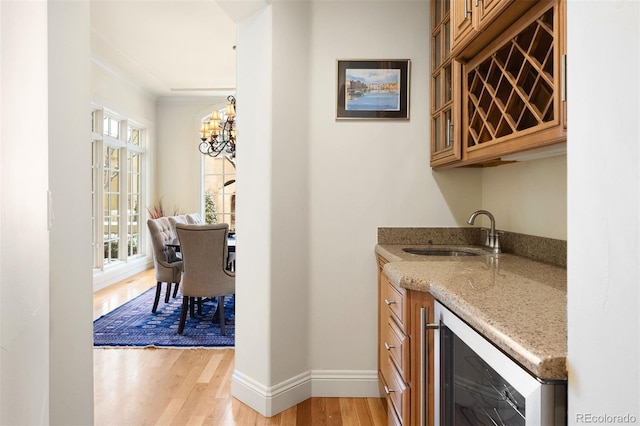 bar with beverage cooler, a sink, baseboards, light wood-style floors, and indoor wet bar