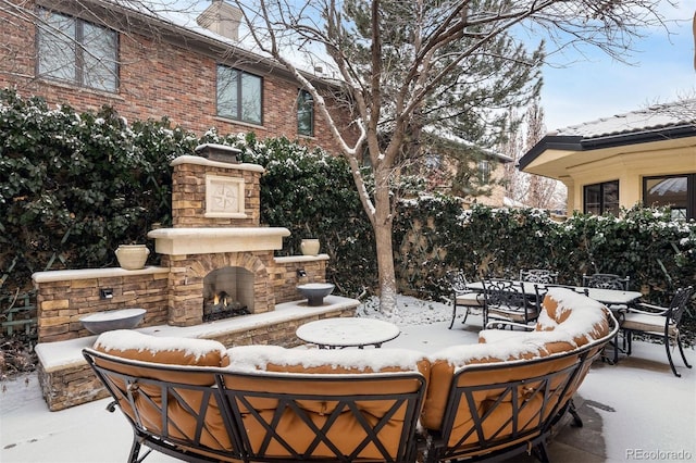 snow covered patio featuring an outdoor stone fireplace