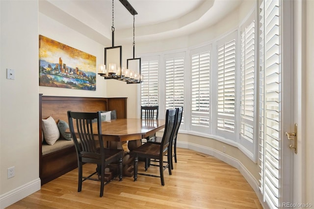 dining area with a raised ceiling, a notable chandelier, light wood-style flooring, and baseboards