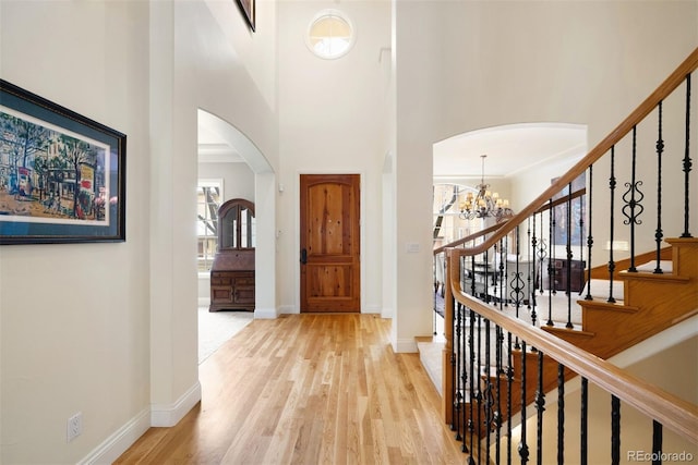 foyer with a towering ceiling, light wood-style flooring, arched walkways, and baseboards