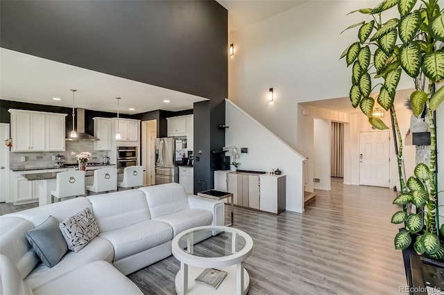 living room featuring light wood-style floors, a towering ceiling, stairway, baseboards, and recessed lighting