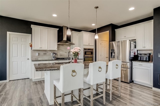 kitchen with wall chimney exhaust hood, stainless steel appliances, a kitchen bar, light wood finished floors, and recessed lighting