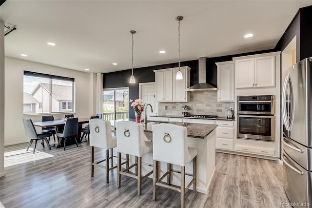 kitchen with stainless steel appliances, wall chimney exhaust hood, a sink, light wood-type flooring, and a breakfast bar area