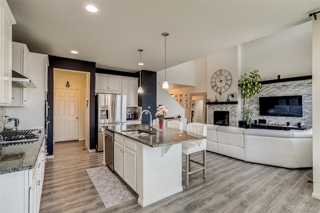 kitchen featuring a sink, a kitchen bar, light wood-style flooring, dark stone counters, and recessed lighting