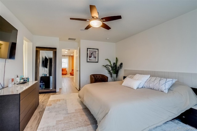 bedroom with light wood-type flooring, ceiling fan, and ensuite bath