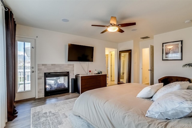 bedroom featuring access to exterior, light wood-style floors, a fireplace, and ceiling fan