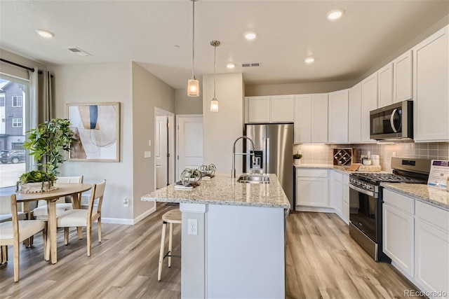 6807 Huddersfield Ln, Castle Pines, CO 80108 - kitchen featuring appliances with stainless steel finishes, a sink, light wood finished floors, tasteful backsplash, and visible vents