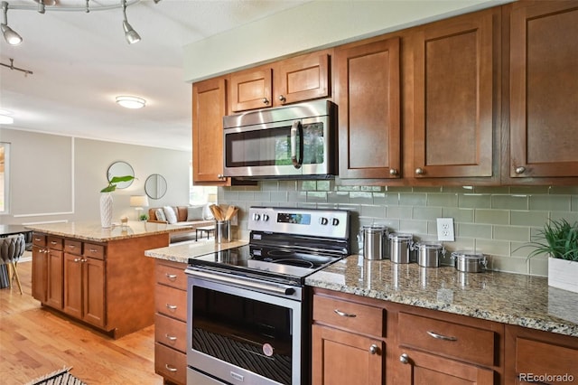 1646 S Stuart St, Denver, CO 80219 - kitchen featuring stainless steel appliances, light wood-style flooring, brown cabinetry, backsplash, and light stone counters