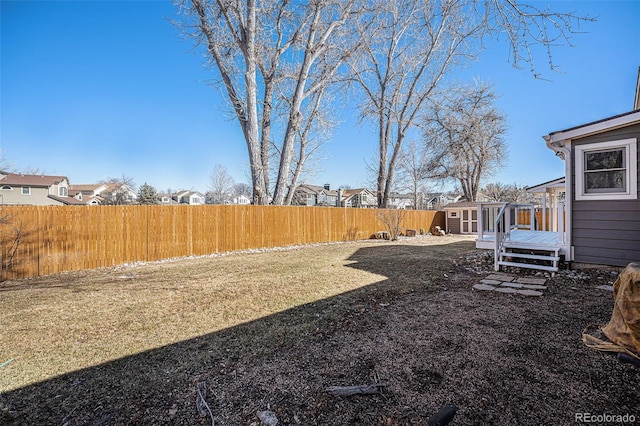 view of yard featuring a residential view, a fenced backyard, an outdoor structure, and a wooden deck