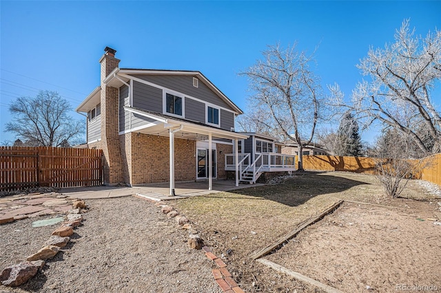 rear view of house featuring a fenced backyard, a chimney, a patio, and brick siding