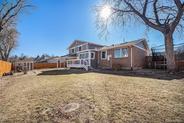 back of property featuring a trampoline, brick siding, a yard, and a fenced backyard