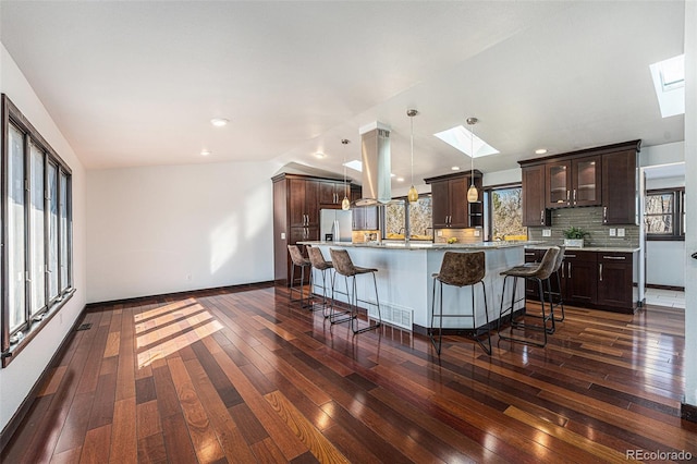 kitchen with lofted ceiling with skylight, stainless steel fridge, dark brown cabinetry, and decorative backsplash