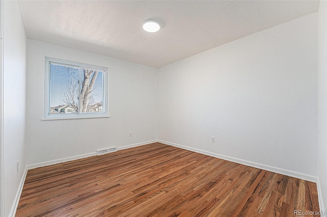 spare room with baseboards, visible vents, and wood finished floors