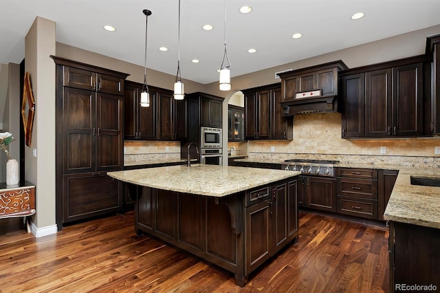 14022 E Fair Pl, Centennial, CO 80111 - kitchen featuring appliances with stainless steel finishes, an island with sink, recessed lighting, dark brown cabinetry, and light stone counters