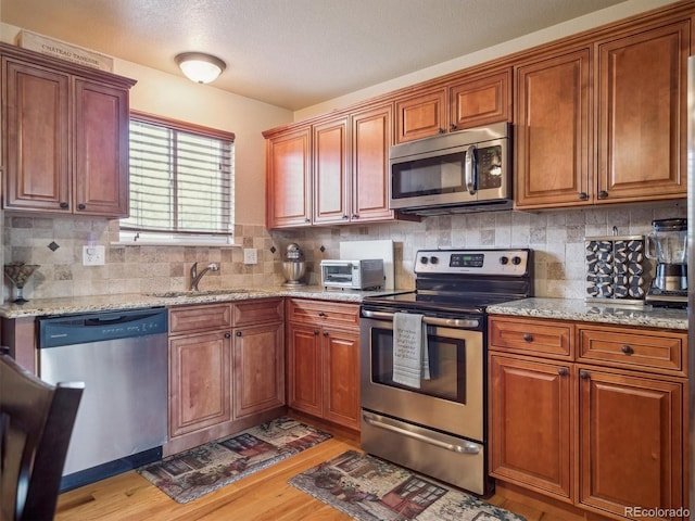 kitchen featuring tasteful backsplash, light stone counters, a sink, light wood-style flooring, and appliances with stainless steel finishes