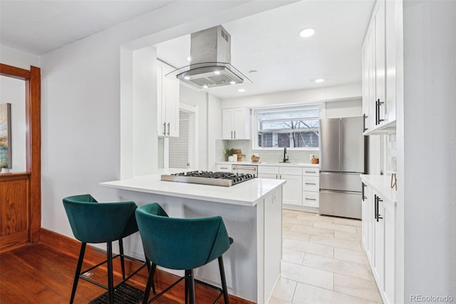 kitchen featuring a breakfast bar area, island range hood, white cabinetry, and appliances with stainless steel finishes