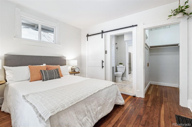 bedroom featuring a barn door, a closet, ensuite bath, and dark wood-type flooring