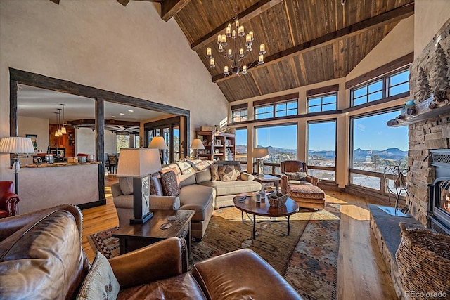 living room featuring a mountain view, a stone fireplace, high vaulted ceiling, a chandelier, and beam ceiling