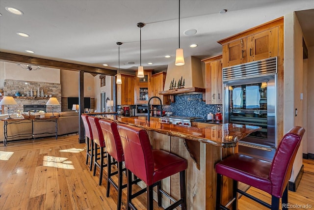 kitchen featuring custom exhaust hood, light hardwood / wood-style floors, a kitchen bar, built in fridge, and hanging light fixtures